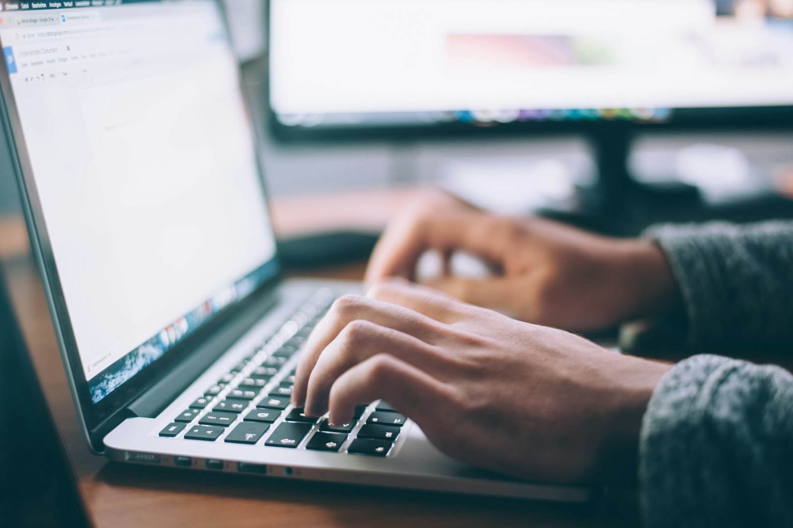 Person typing on a laptop at a desk with a notebook nearby