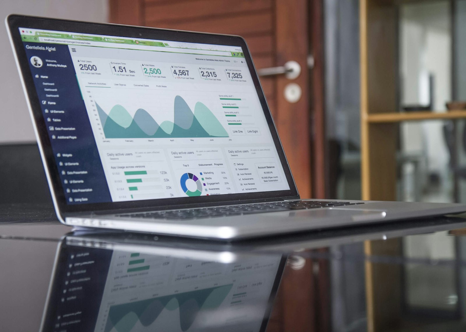 Laptop on a glass-top table displaying analytics charts.